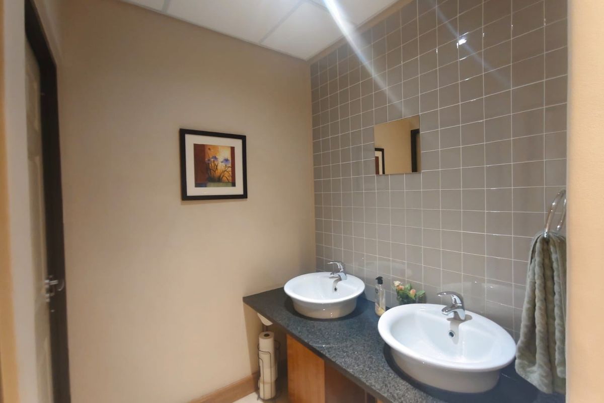 A functional commercial bathroom featuring a double vanity with granite countertops, ceramic tile backsplash, and modern drop-in sinks.