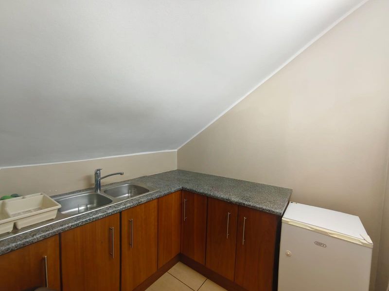 A compact scullery area featuring wood-finish cabinetry, granite countertops, and a double bowl stainless steel sink set under a sloped ceiling.