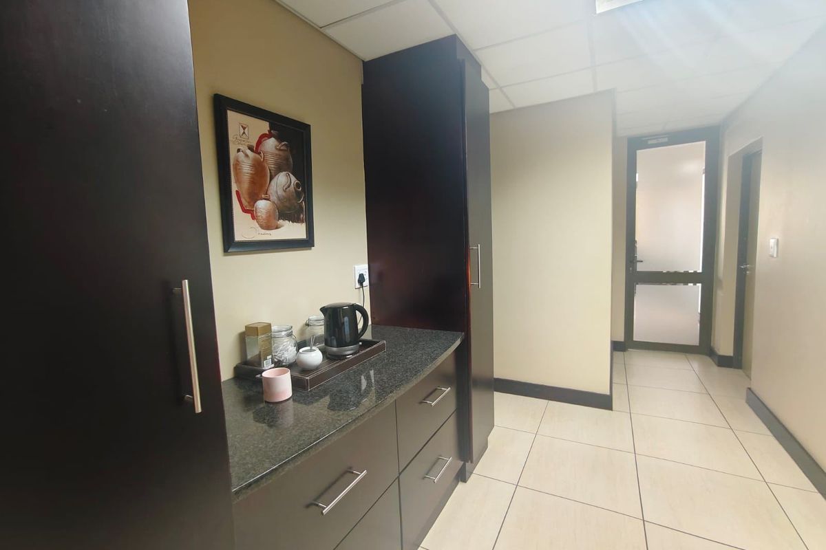 A compact kitchenette area featuring dark wood cabinetry, granite countertops, and tiled flooring, leading into a hallway with a glass-paneled door.