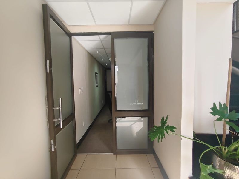 A clean, professional commercial hallway featuring tiled flooring, a suspended ceiling with recessed lighting, and a modern frosted glass aluminium door.