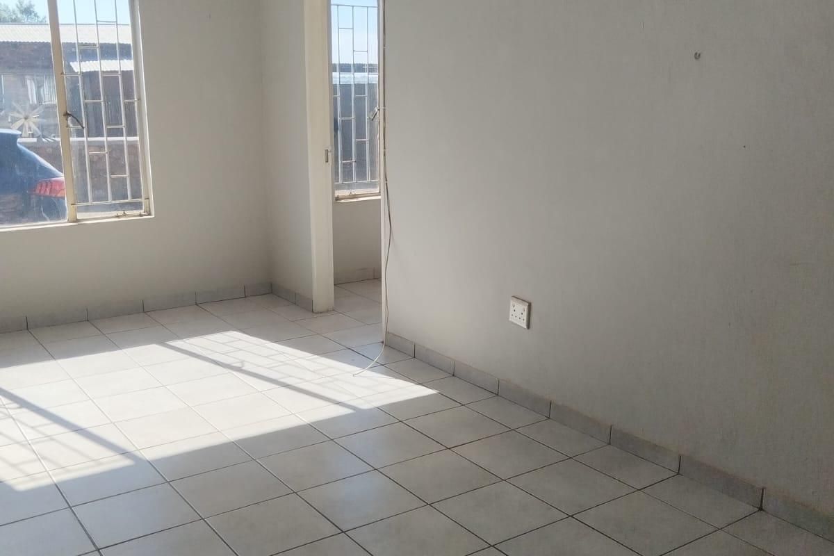 An empty living area featuring tiled flooring, security bars on windows, and neutral wall finishes, offering a blank canvas for potential interior design.
