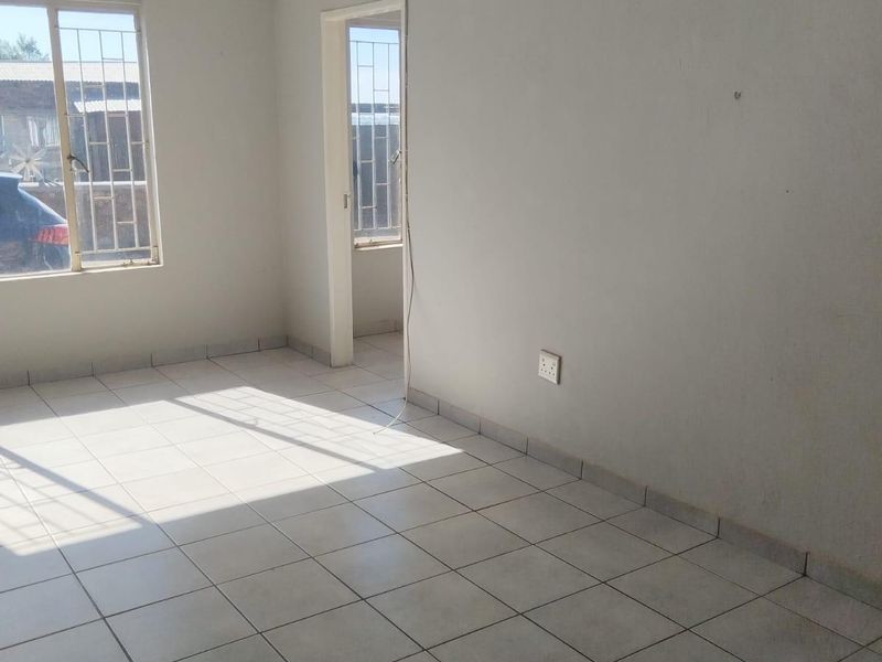 An empty living area featuring tiled flooring, security bars on windows, and neutral wall finishes, offering a blank canvas for potential interior design.