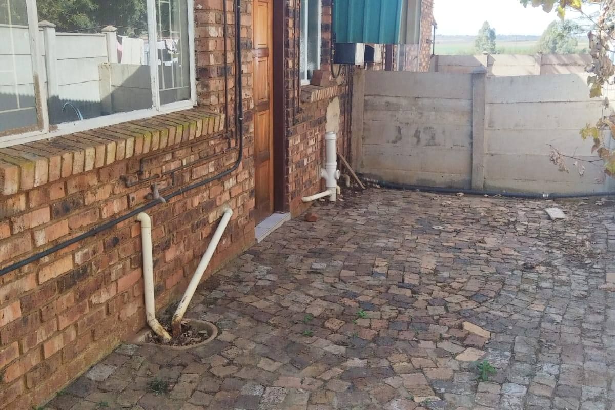 Rear exterior view of a face brick house featuring a paved patio area and precast concrete boundary walling.