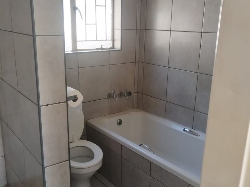 A functional bathroom featuring a bathtub, toilet, and full-height wall tiling. The space is ready for a modern update to refresh the dated finishes.