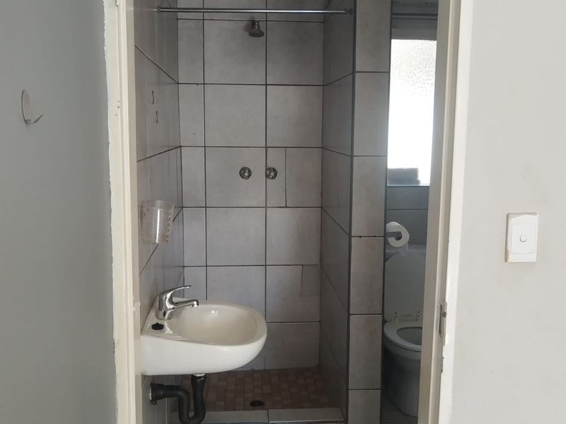 A compact bathroom featuring a tiled shower enclosure, wall-mounted basin, and toilet, requiring some cosmetic updates to improve its overall condition.