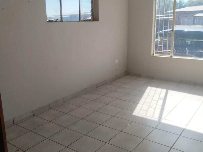 An empty living room featuring neutral tiled flooring, large windows with security bars, and plain walls, offering a blank canvas for interior design.