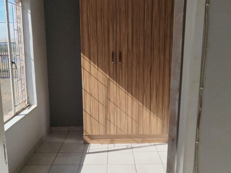 A bright, empty bedroom featuring tiled flooring and a built-in wooden wardrobe, offering a clean and functional space ready for personalization.