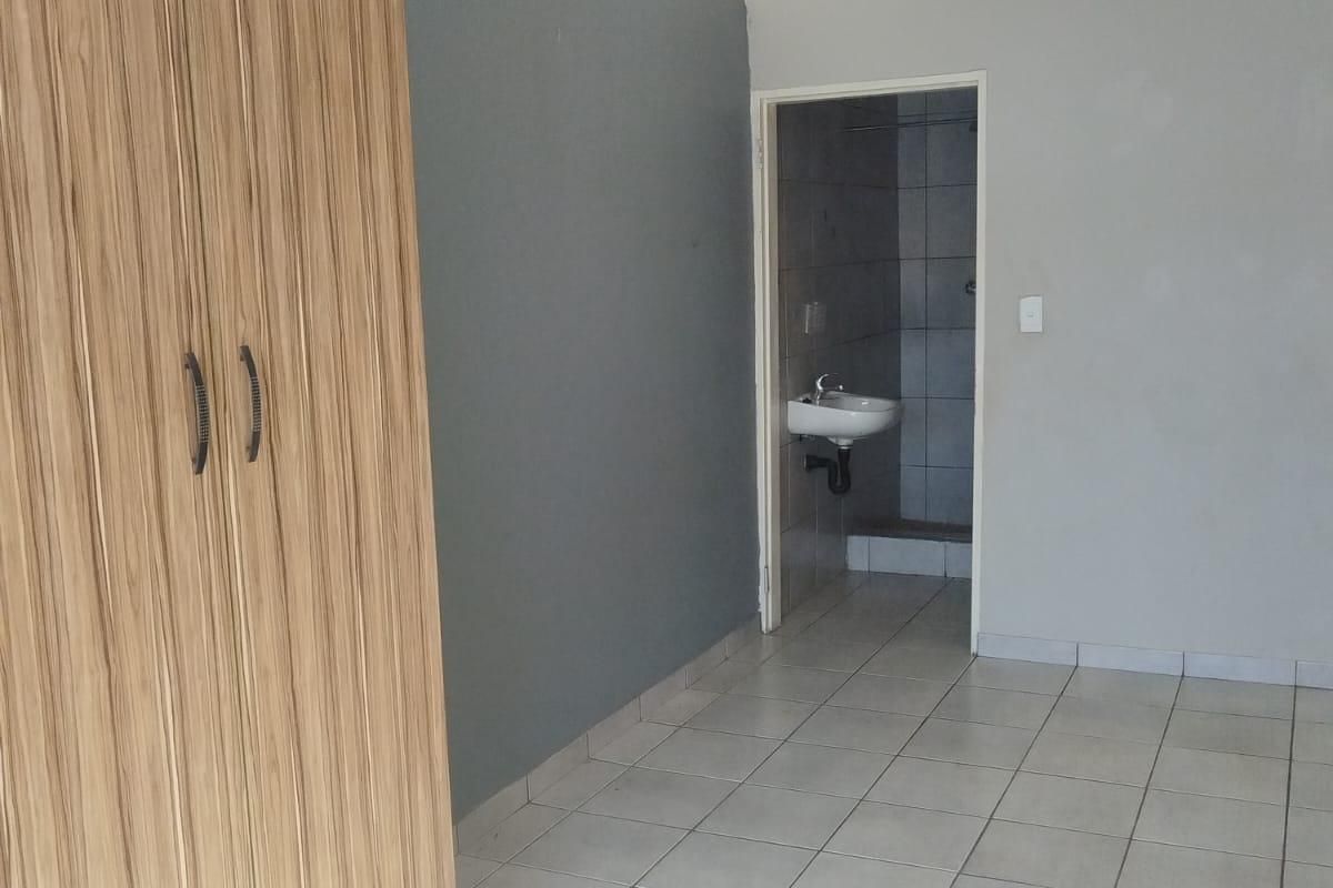 A simple bedroom featuring tiled flooring, a built-in wooden wardrobe, and direct access to an en-suite bathroom.