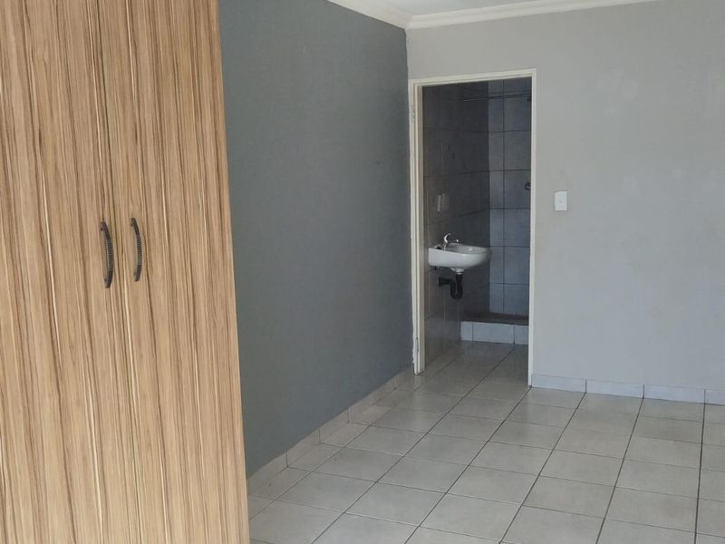 A simple bedroom featuring tiled flooring, a built-in wooden wardrobe, and direct access to an en-suite bathroom.