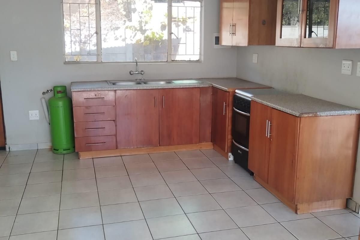 A functional kitchen featuring wooden cabinetry, laminate countertops, a stainless steel sink, and tiled flooring, offering a clean and practical workspace.