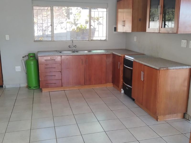A functional kitchen featuring wooden cabinetry, laminate countertops, a stainless steel sink, and tiled flooring, offering a clean and practical workspace.
