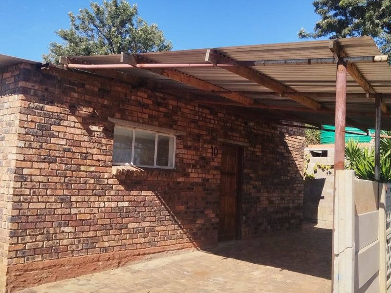Front exterior view of a face brick house featuring a paved driveway and a corrugated metal carport structure.