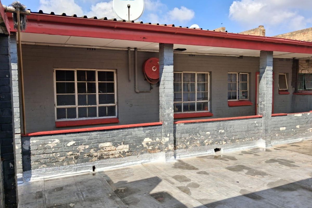 Exterior rear view of a commercial building featuring a concrete patio, brick masonry walls, steel windows, and a mounted fire hose reel.