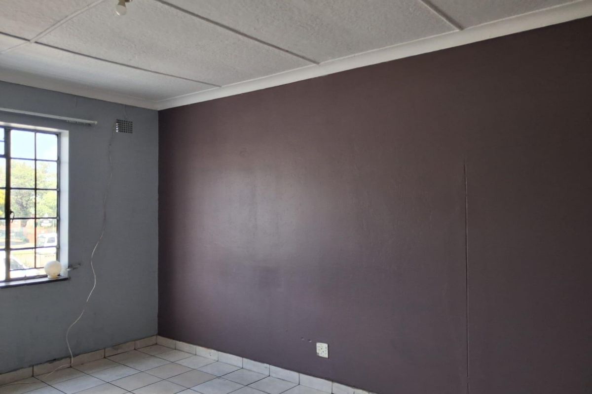 An empty room featuring tiled flooring, a steel-framed window, and a dark accent wall with visible surface imperfections.