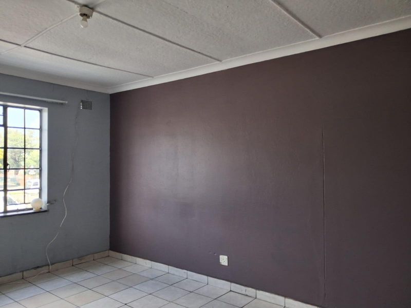 An empty room featuring tiled flooring, a steel-framed window, and a dark accent wall with visible surface imperfections.