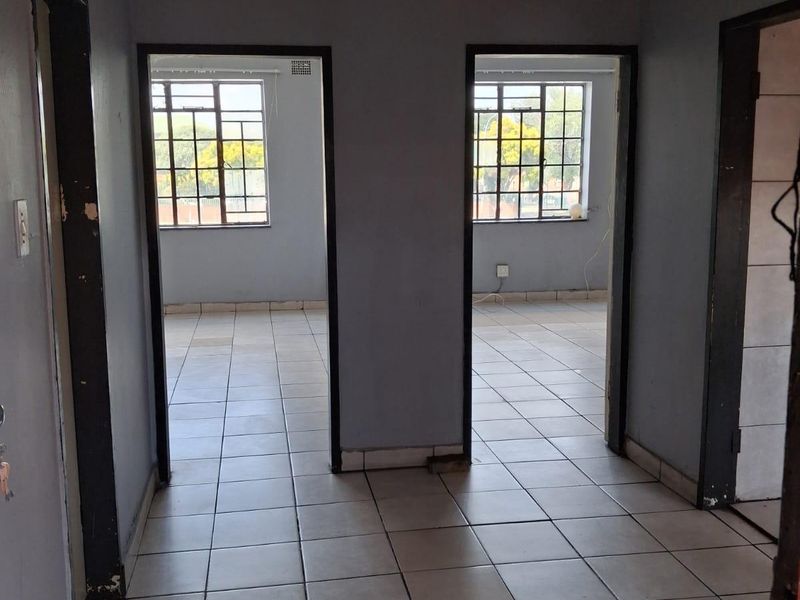 A vacant hallway featuring tiled flooring and two doorways leading into adjacent rooms with steel-framed windows.