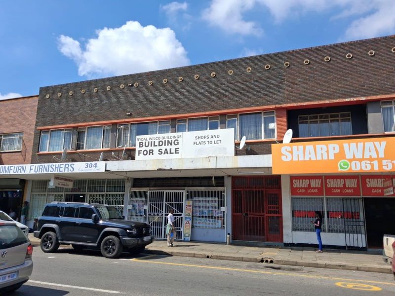 Street-level view of a multi-story commercial building featuring ground-floor retail storefronts with security gates and upper-level residential or office windows.