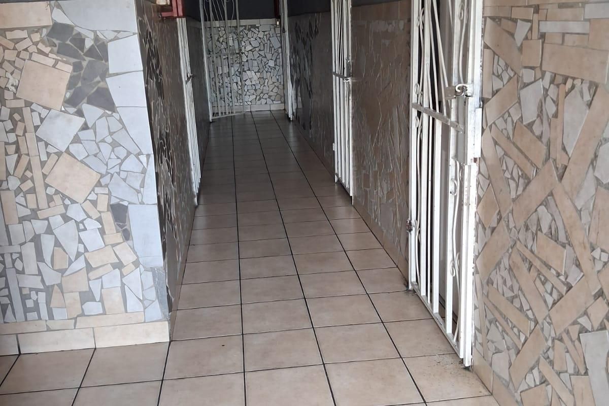 A commercial hallway featuring ceramic floor tiles, mosaic wall detailing, and multiple security gates leading to individual units.