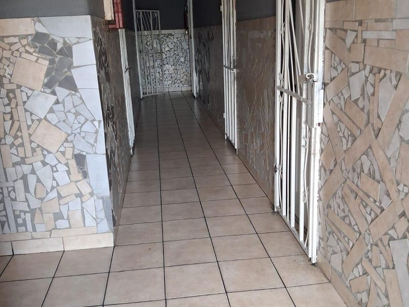 A commercial hallway featuring ceramic floor tiles, mosaic wall detailing, and multiple security gates leading to individual units.