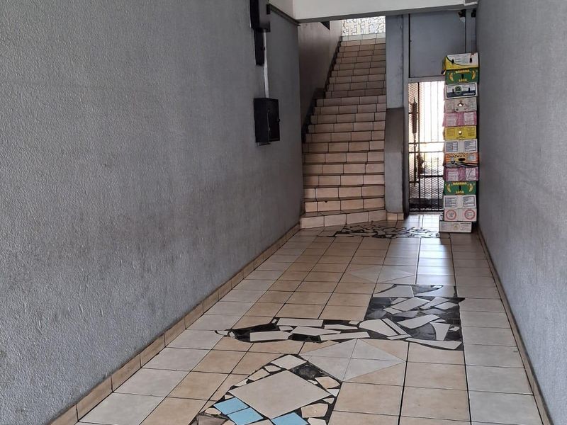 A commercial hallway featuring tiled flooring with decorative inlays, leading to a staircase and a secure metal gate entrance.