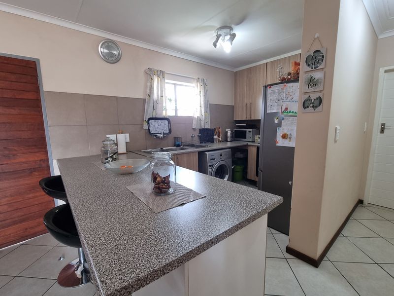 Functional kitchen featuring laminate cabinetry, a breakfast bar, tiled backsplash, and ceramic floor tiles, offering a practical layout for daily use.