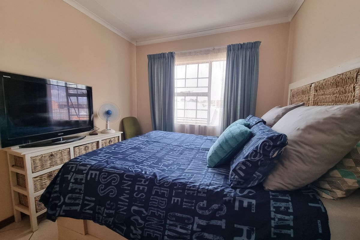 A functional bedroom featuring tiled flooring, a window with security bars, and coved ceiling detailing.