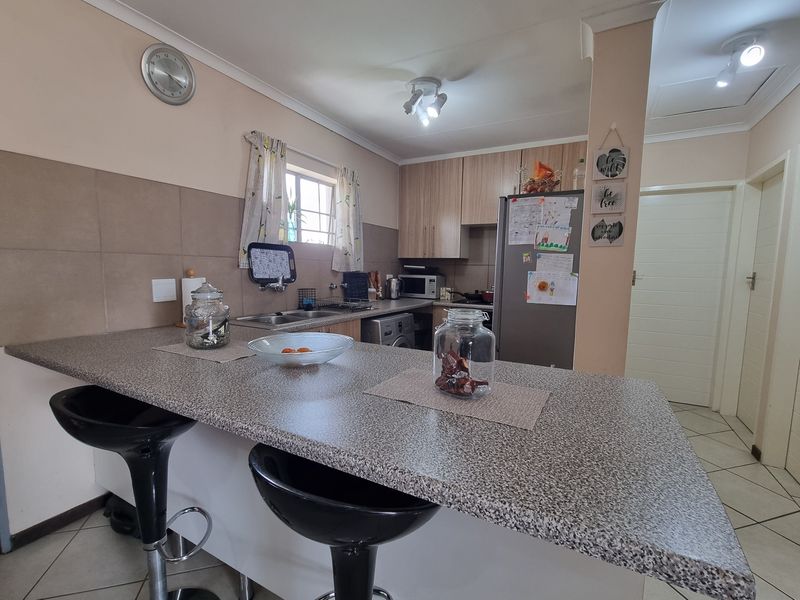 A functional kitchen featuring laminate cabinetry, a spacious breakfast bar with granite-look countertops, tiled backsplash, and ceramic floor tiles.