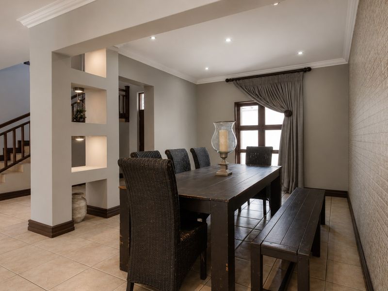 A well-maintained dining area featuring tiled floors, recessed lighting, built-in display shelving, and a staircase with a wooden balustrade.