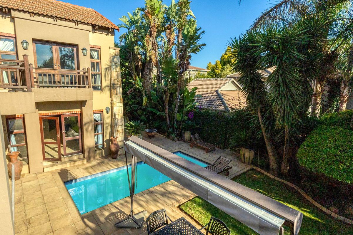 Rear exterior view featuring a swimming pool, paved patio area, and a two-story house facade with a balcony and stone accents.