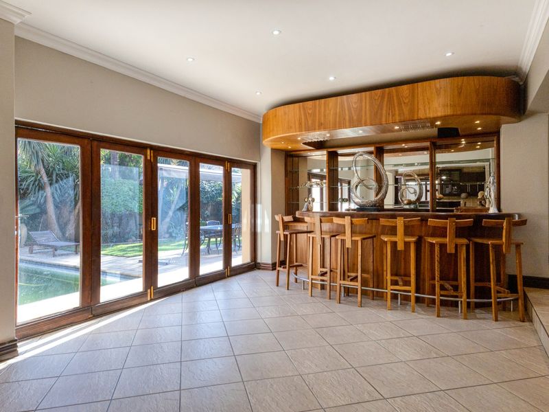 Spacious entertainment area featuring a custom built-in wooden bar with mirrored shelving, recessed lighting, and large folding doors opening to the pool area.