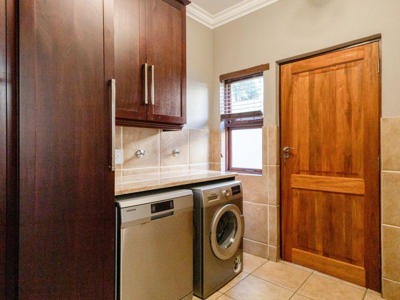 Functional laundry room featuring built-in dark wood cabinetry, stone countertops, tiled splashbacks, and dedicated plumbing connections for appliances.