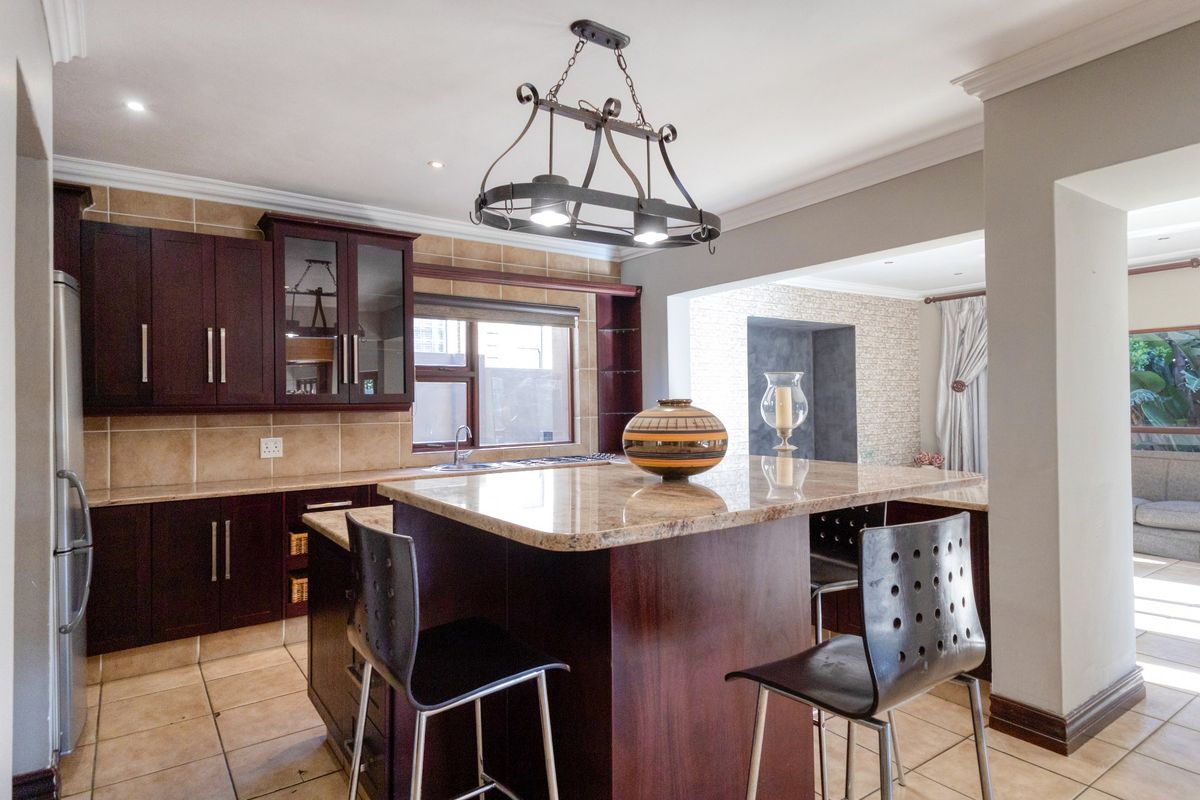 A well-appointed kitchen featuring dark wood cabinetry, granite countertops, a central island, and tiled flooring, seamlessly flowing into an adjacent living area.