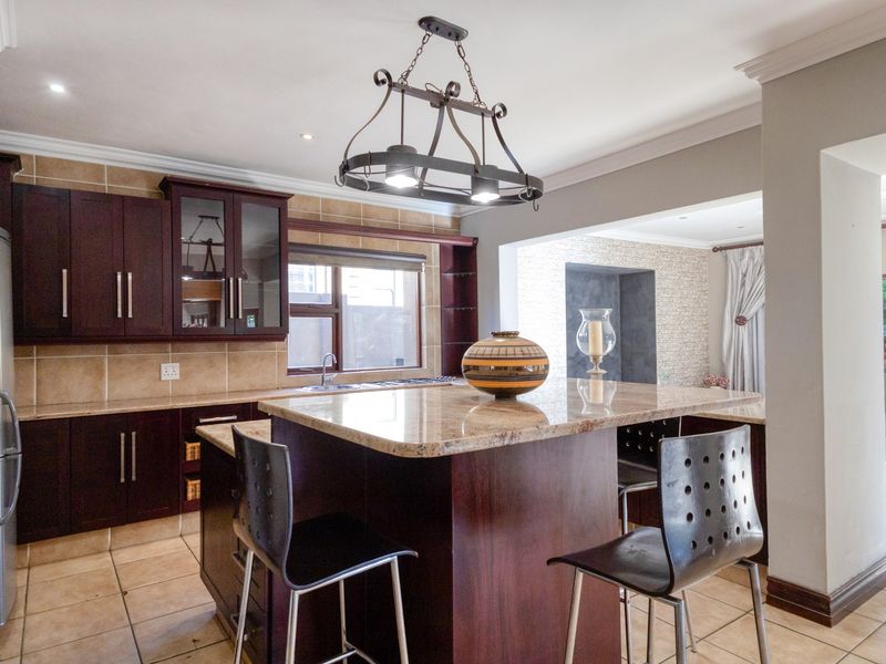 A well-appointed kitchen featuring dark wood cabinetry, granite countertops, a central island, and tiled flooring, seamlessly flowing into an adjacent living area.