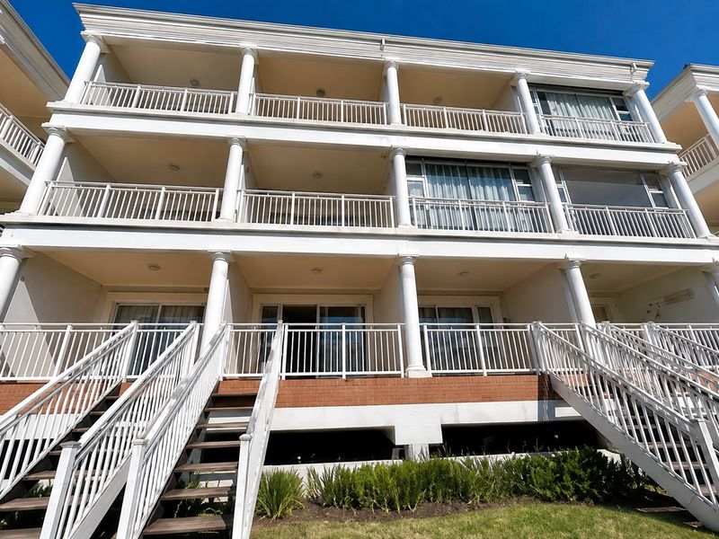 A low-angle view of a multi-story apartment building featuring stacked balconies with classical columns, metal railings, and external staircases leading to the ground level.