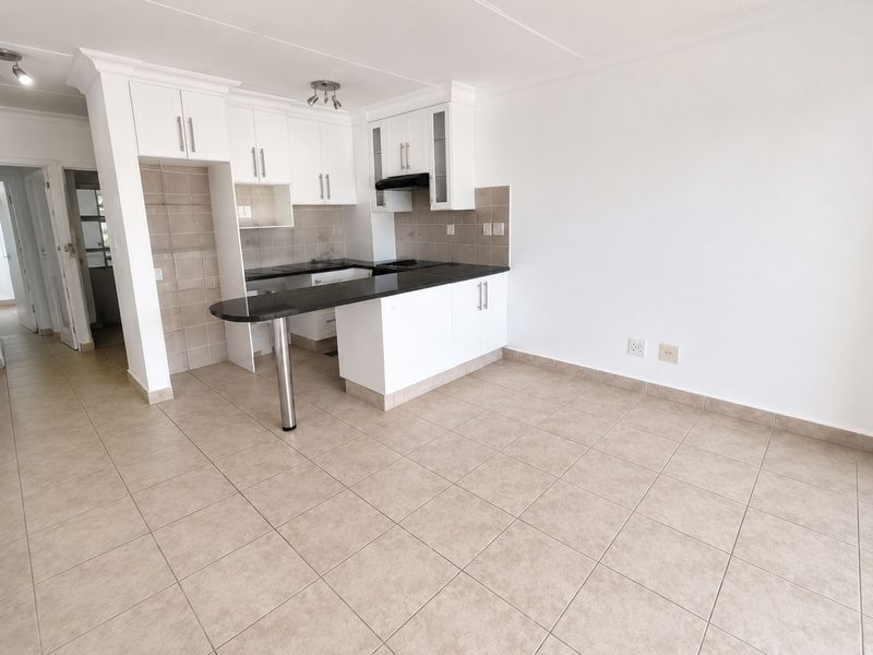 An open-plan kitchen area featuring white cabinetry, dark granite countertops, a breakfast bar, and neutral tiled flooring in a clean, vacant space.