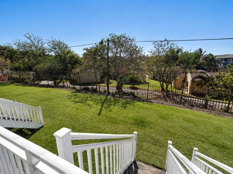 A well-maintained garden area featuring a timber staircase with white balustrades, overlooking a grassy lawn and secure metal perimeter fencing.
