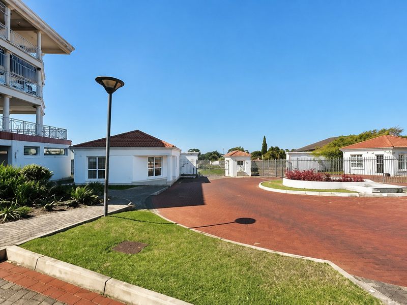 The entrance area of the apartment complex features a paved driveway, a security gatehouse, and well-maintained landscaped grounds.
