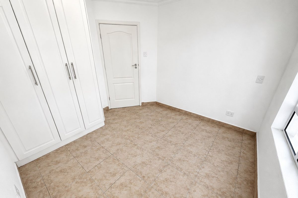 A clean, empty bedroom featuring neutral tiled flooring and white built-in cupboards, offering a blank canvas for personalization.