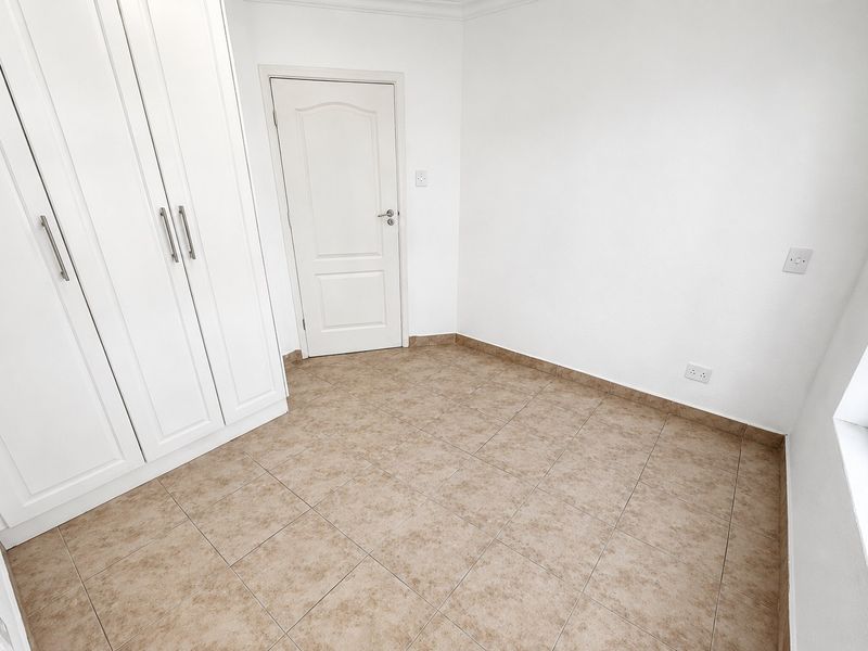 A clean, empty bedroom featuring neutral tiled flooring and white built-in cupboards, offering a blank canvas for personalization.