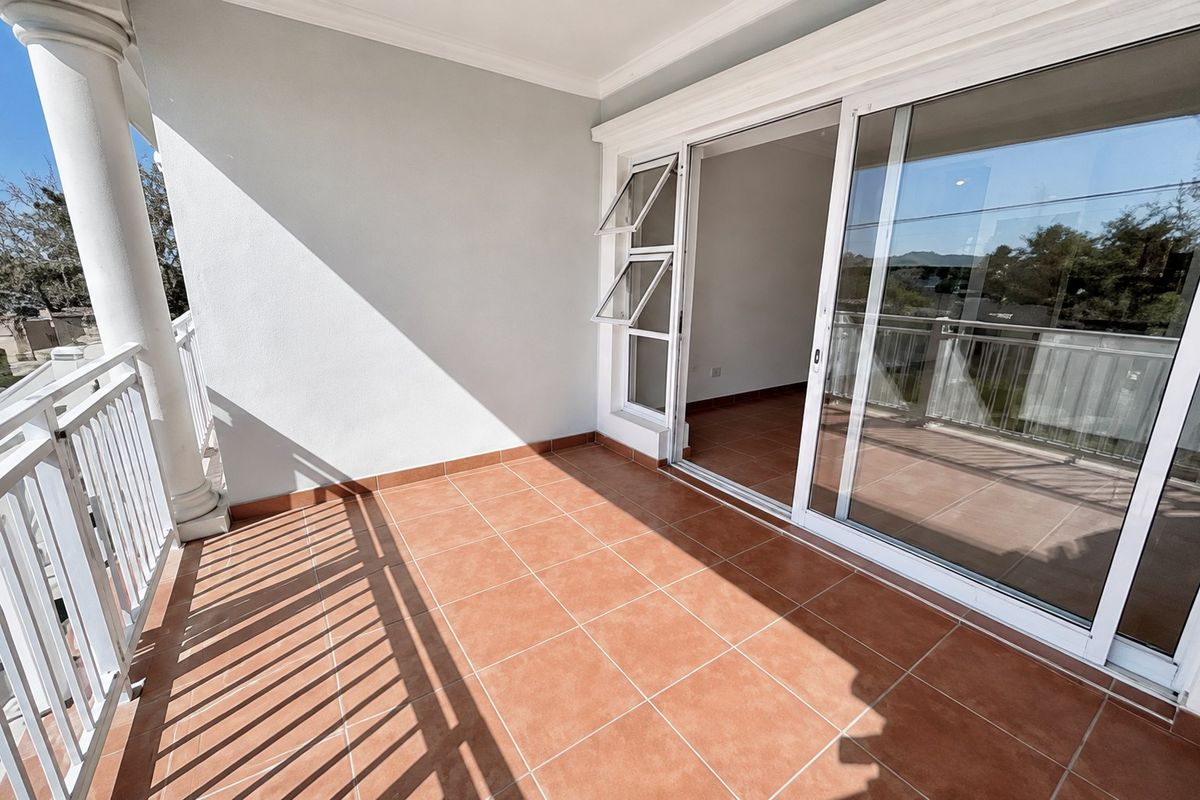 A spacious, tiled balcony featuring a white railing, a structural column, and large sliding glass doors providing access to the interior living space.