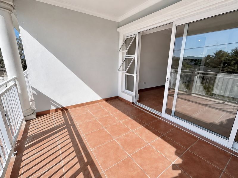 A spacious, tiled balcony featuring a white railing, a structural column, and large sliding glass doors providing access to the interior living space.