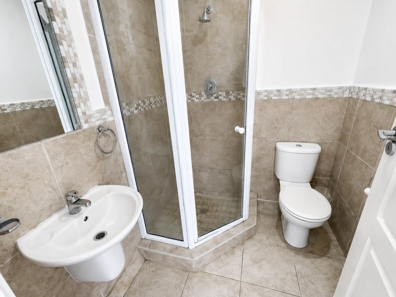 A clean, functional bathroom featuring a corner shower enclosure, pedestal basin, and toilet with neutral tiled finishes.