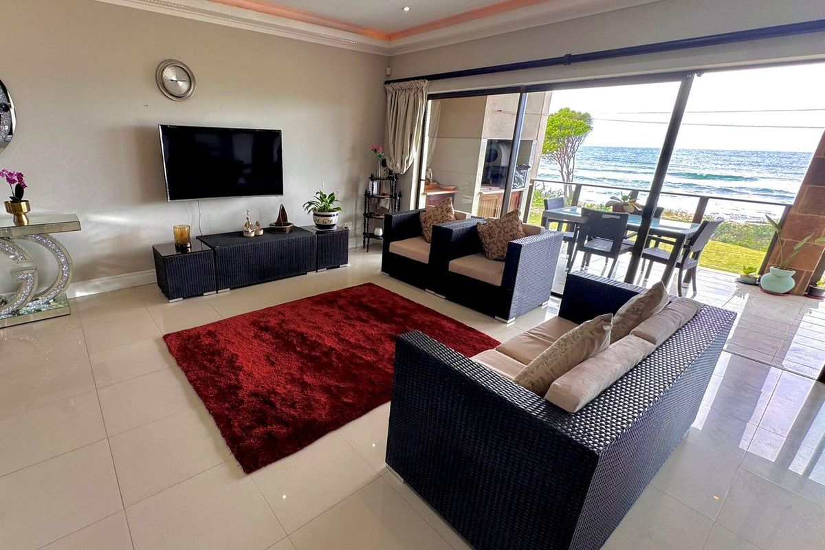 Spacious living room featuring large sliding glass doors that open to a balcony with ocean views, complemented by recessed and cove lighting.