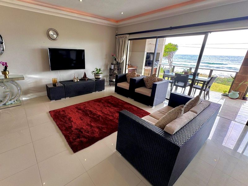 Spacious living room featuring large sliding glass doors that open to a balcony with ocean views, complemented by recessed and cove lighting.