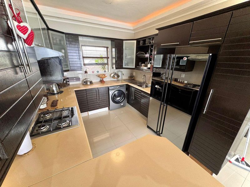 Modern kitchen featuring dark cabinetry, stone countertops, integrated gas hob, extractor fan, and tiled flooring with ample storage space.