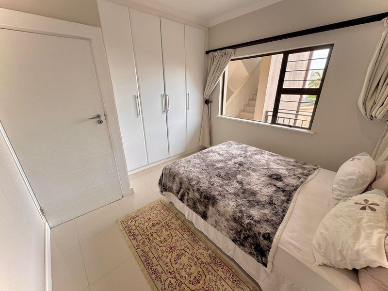 A well-maintained bedroom featuring built-in cupboards, tiled flooring, and a window with security bars, offering a clean and functional living space.