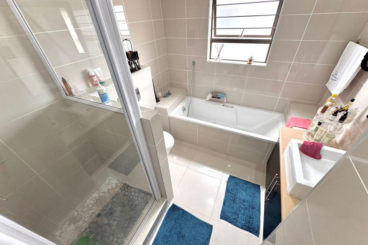 A functional bathroom featuring a glass-enclosed shower, a built-in bathtub, and a vanity basin with neutral wall and floor tiling.
