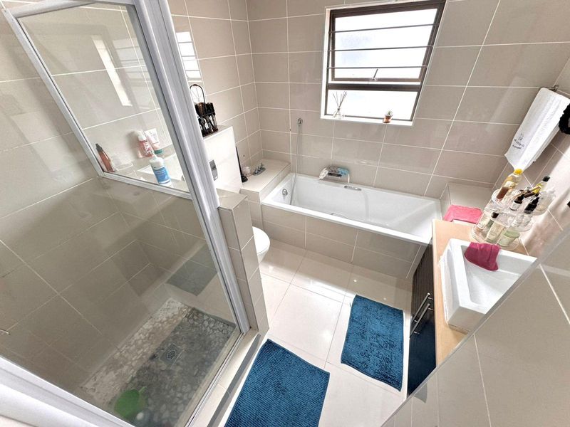 A functional bathroom featuring a glass-enclosed shower, a built-in bathtub, and a vanity basin with neutral wall and floor tiling.