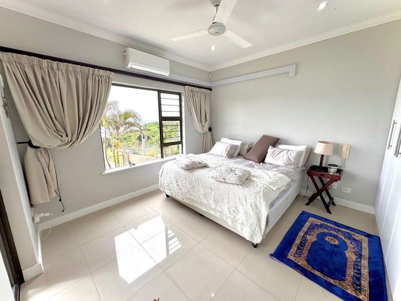 A bright bedroom featuring tiled flooring, a ceiling fan, a split-system air conditioner, and a large window with views.