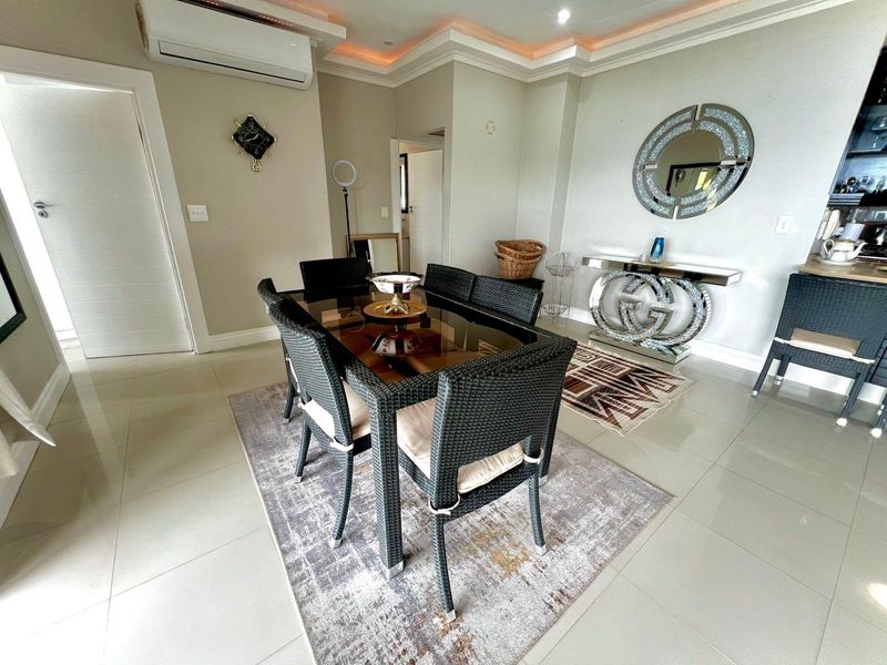 A well-maintained dining area featuring tiled flooring, recessed ceiling lighting with cove accents, and a wall-mounted split-system air conditioner.